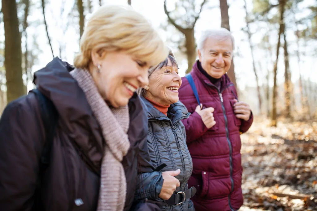 Senior man and women walking together through forest trail on a cold autumn day.