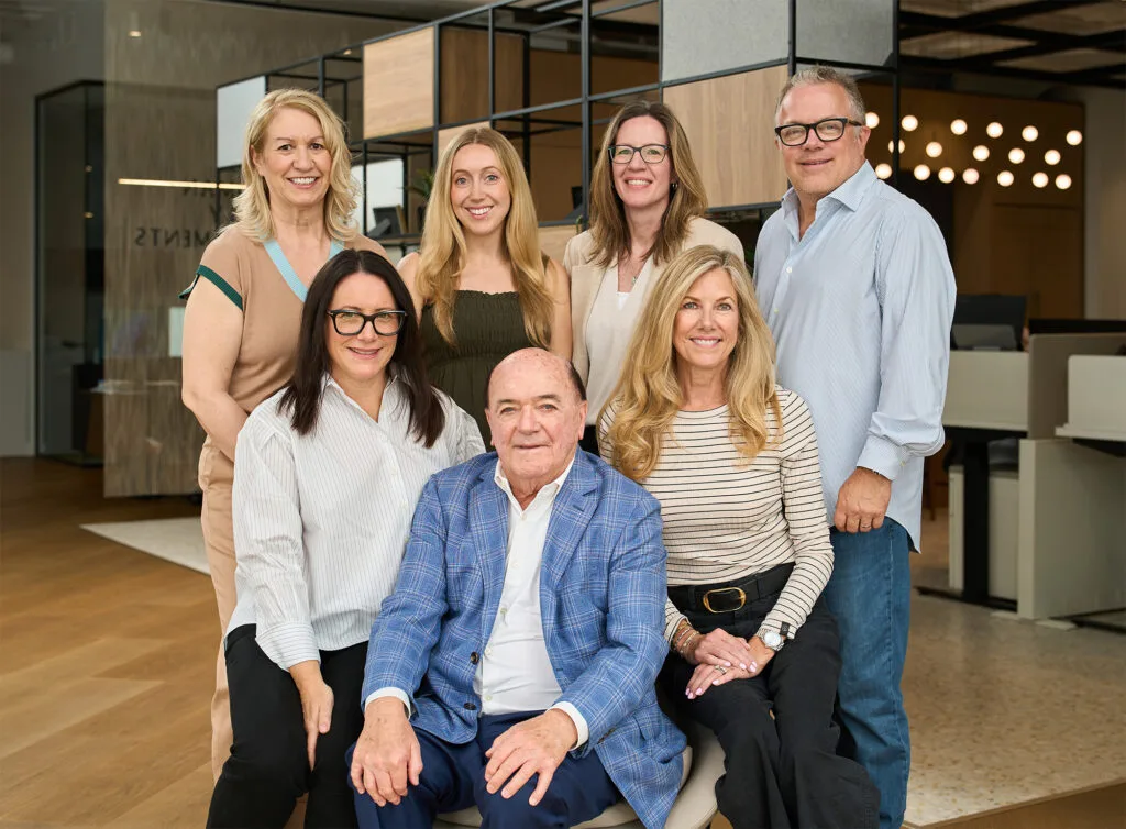 Six members of The Jessiman Foundation and the Alzheimer Society of Manitoba's CEO, Erin Crawford, standing and sitting in warm, neutral coloured clothing.